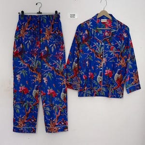 May include: Blue pajama set with a floral and bird print. The set includes a long-sleeved button-down shirt and matching pants. The shirt and pants have white trim. The text "FUTURE TEXTILE" is visible on a small tag.