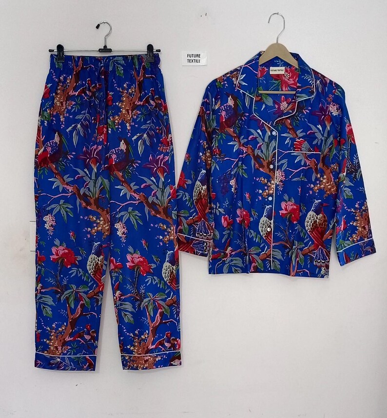 May include: Blue pajama set with a floral and bird print. The set includes a long-sleeved button-down shirt and matching pants. The shirt and pants have white trim. The text "FUTURE TEXTILE" is visible on a small tag.