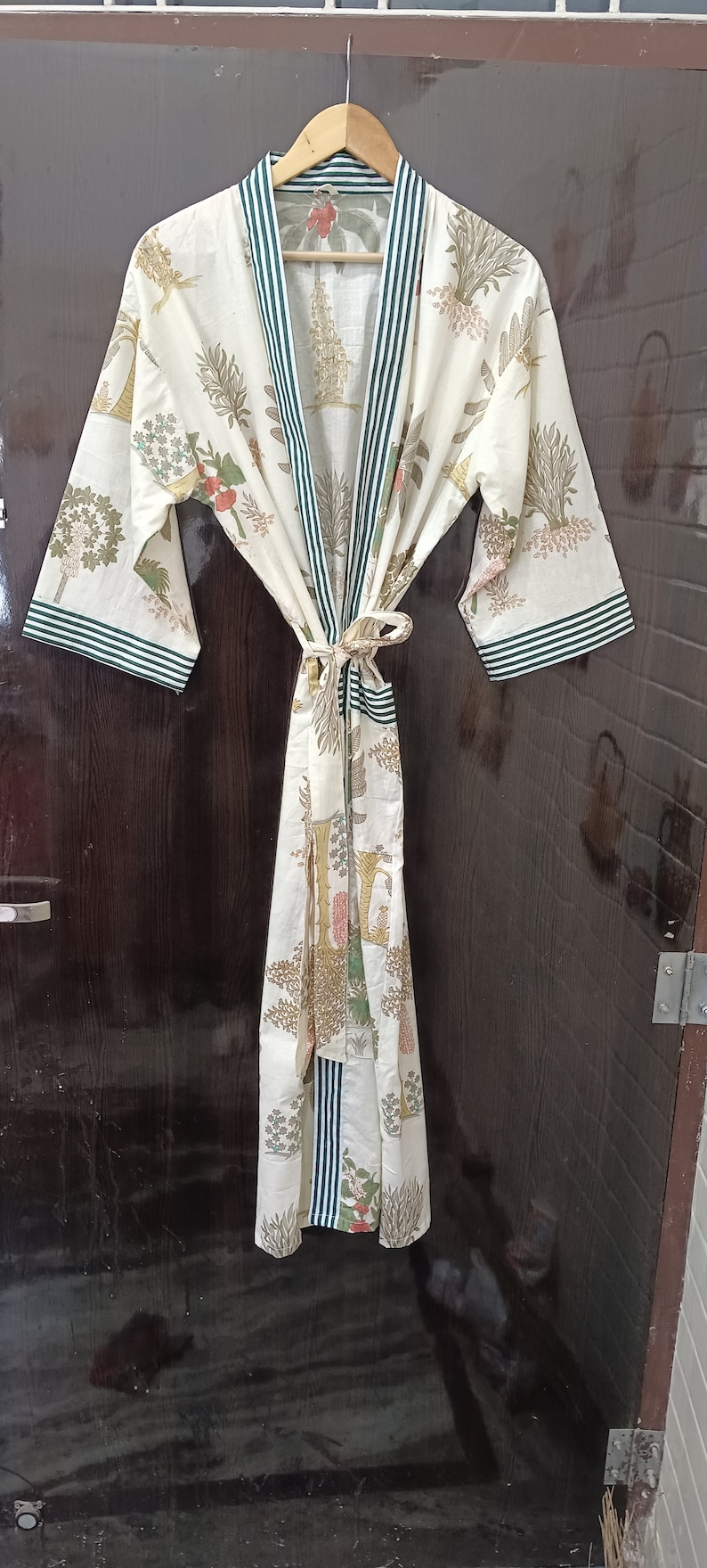 May include: A white cotton robe with a green and white striped trim. The robe features a floral print in a variety of colours, including pink, yellow, and green. The robe is tied at the waist with a matching sash.