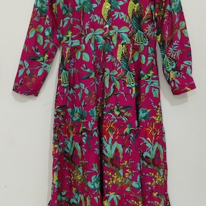 May include: A pink long-sleeved dress with a floral print featuring green leaves, yellow flowers, and colorful birds. The dress has a button-up front and a ruffled hem.