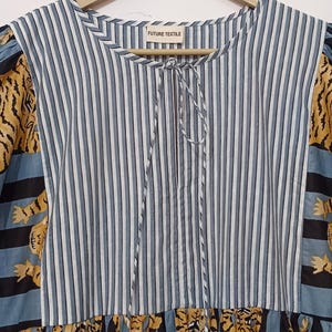 May include: A blue and white striped dress with a tie at the neck. The dress has a patchwork design with tiger print fabric on the sleeves and bottom hem. The dress has the words "FUTURE TEXTILE" on a tag.
