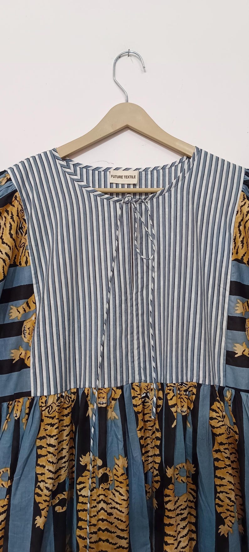 May include: A blue and white striped dress with a tie at the neck. The dress has a patchwork design with tiger print fabric on the sleeves and bottom hem. The dress has the words "FUTURE TEXTILE" on a tag.