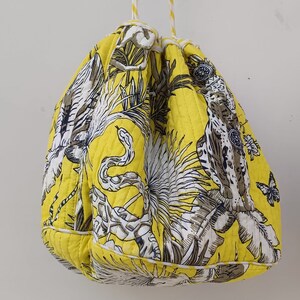 May include: A yellow drawstring bag with a white and black floral print featuring snakes, butterflies, and plants. The bag has a white drawstring.