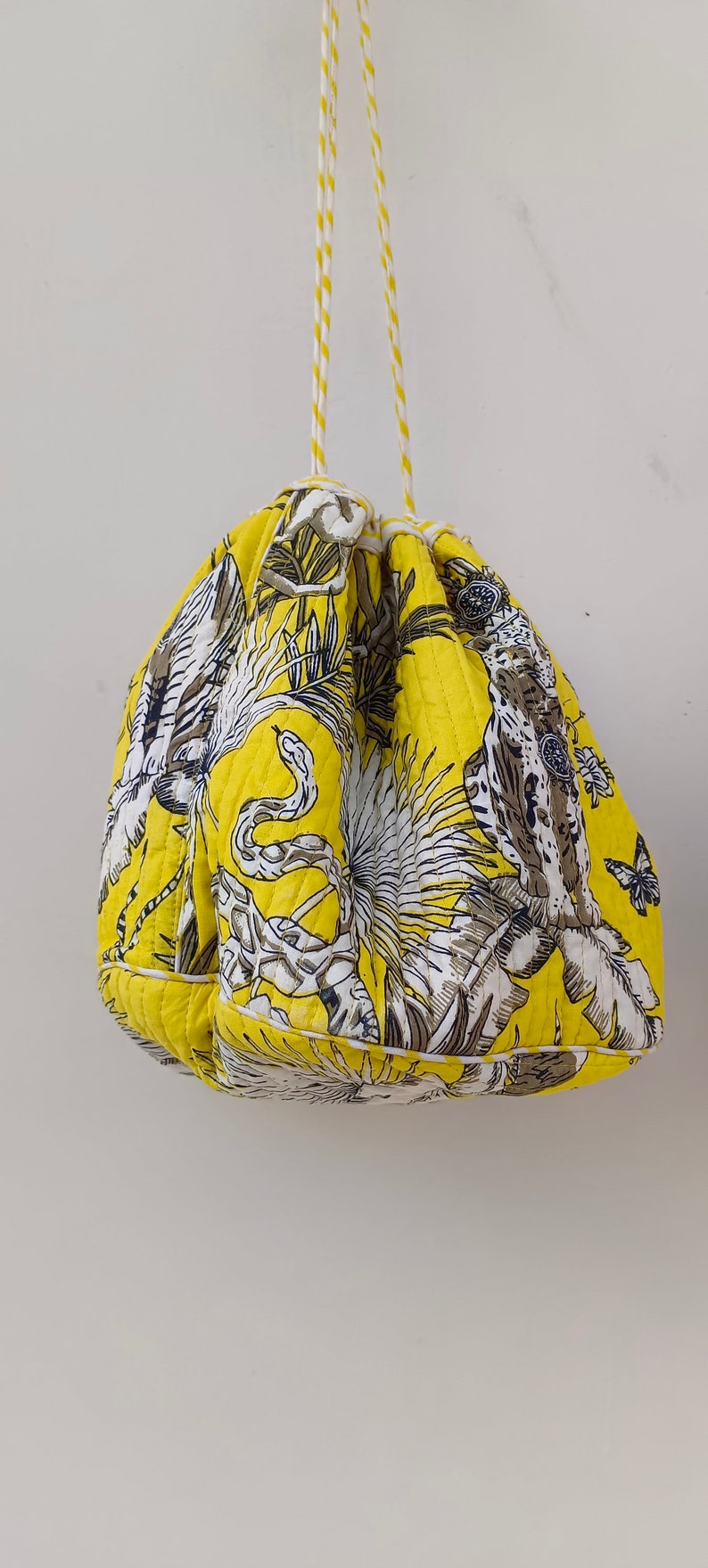 May include: A yellow drawstring bag with a white and black floral print featuring snakes, butterflies, and plants. The bag has a white drawstring.