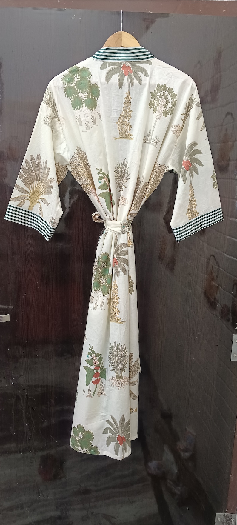 May include: A white cotton robe with a green and white striped trim. The robe features a floral print of palm trees and other tropical plants.
