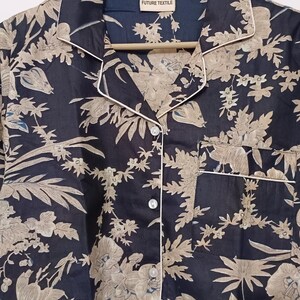 May include: A black button-up shirt with a beige floral print and white piping. The shirt has a collar and a pocket on the left side. The label on the shirt reads "FUTURE TEXTILE".