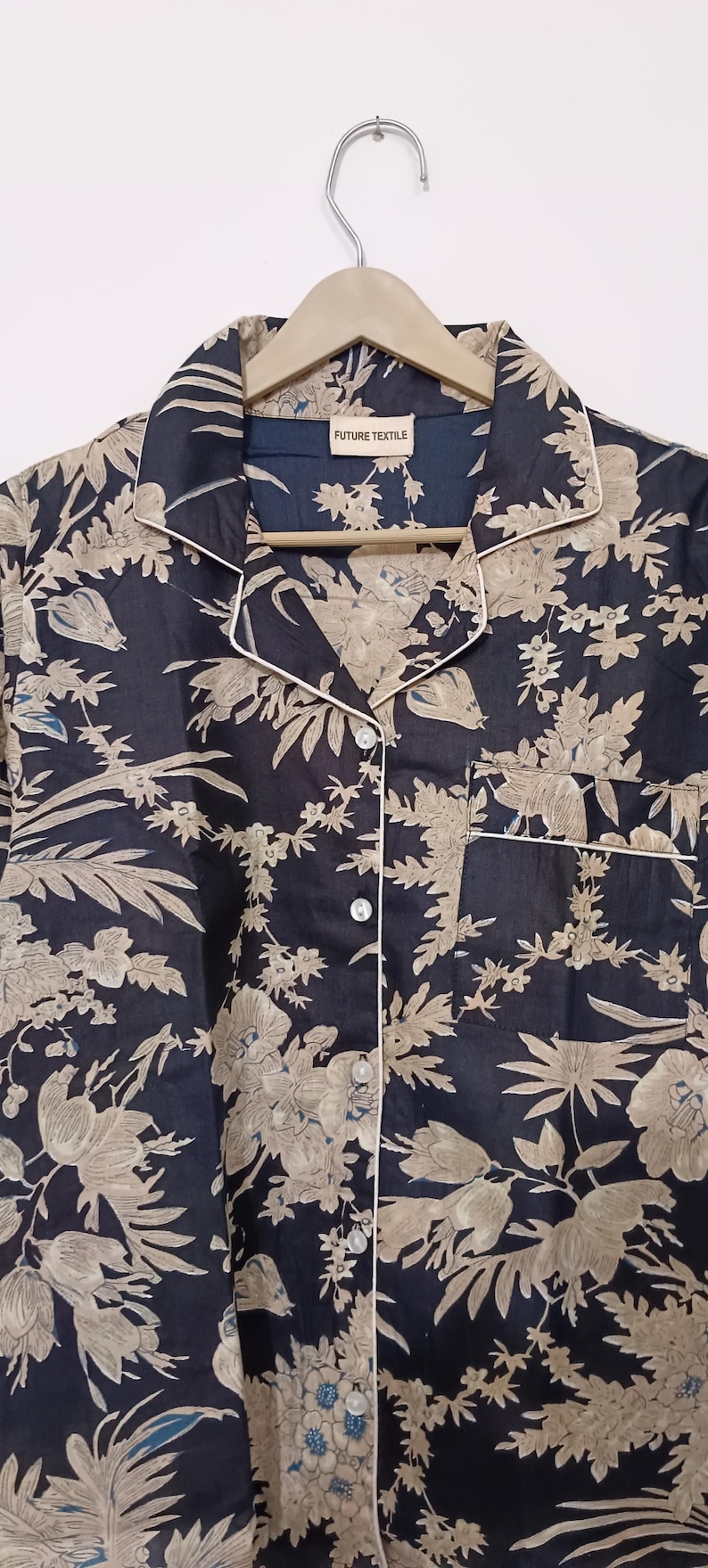 May include: A black button-up shirt with a beige floral print and white piping. The shirt has a collar and a pocket on the left side. The label on the shirt reads "FUTURE TEXTILE".