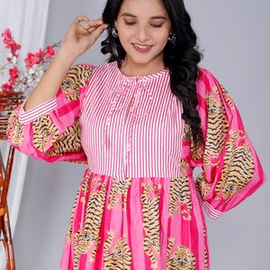 Pu&ograve; includere: Un vestito a righe rosa e bianche con stampa di tigre. Il vestito ha una scollatura rotonda e maniche 3/4. Le maniche sono a sbuffo e hanno una stampa di tigre. Il vestito ha una gonna a pieghe.