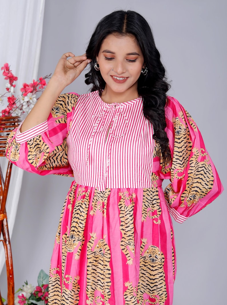 Pu&ograve; includere: Un vestito a righe rosa e bianche con stampa di tigre. Il vestito ha una scollatura rotonda e maniche 3/4. Le maniche sono a sbuffo e hanno una stampa di tigre. Il vestito ha una gonna a pieghe.