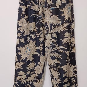 May include: Black pants with a floral print in beige and blue. The pants have a drawstring waist and a white trim.