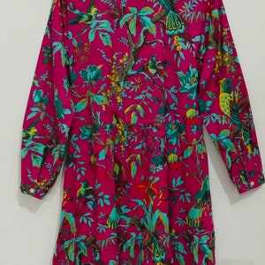 May include: A long-sleeved pink dress with a floral print featuring birds and leaves. The dress has a button-up front and a gathered skirt.