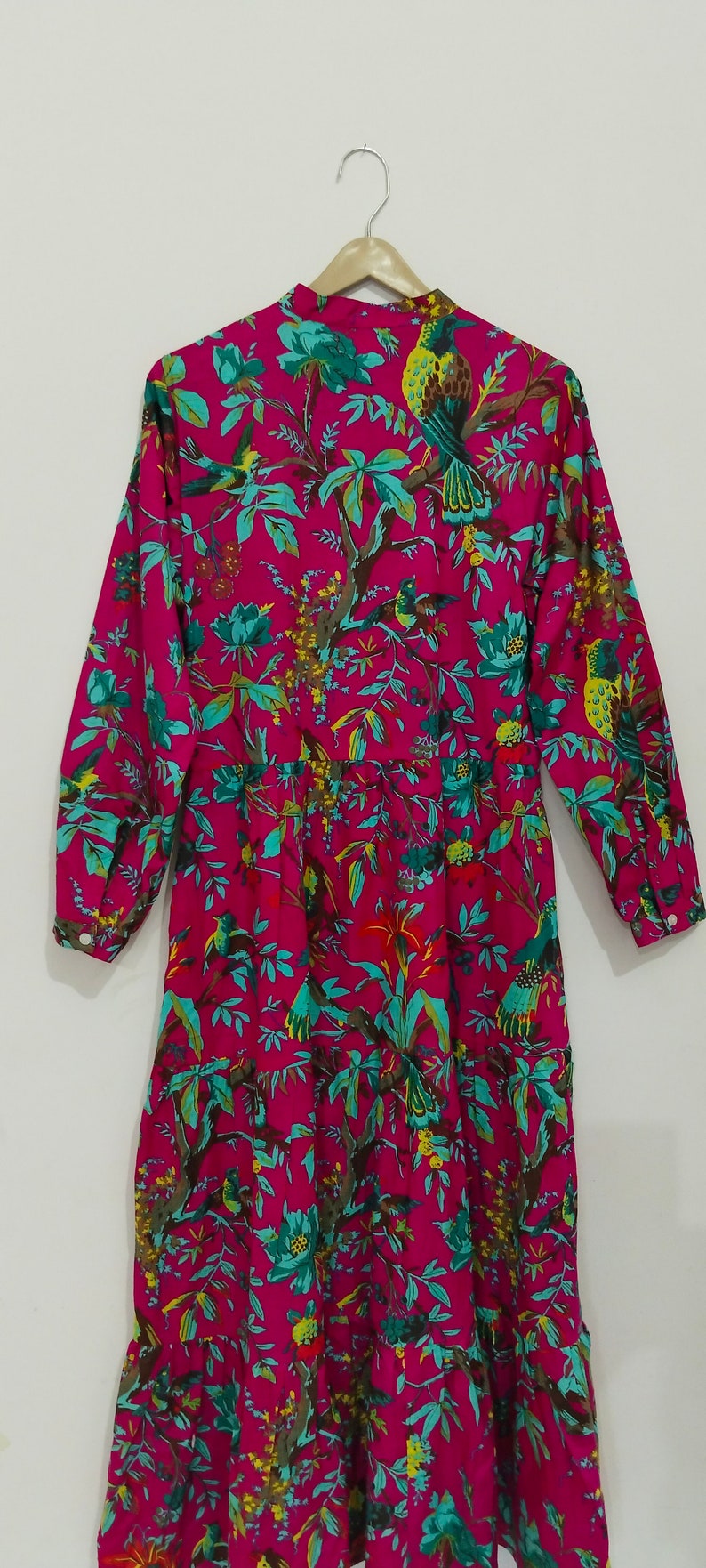 May include: A long-sleeved pink dress with a floral print featuring birds and leaves. The dress has a button-up front and a gathered skirt.
