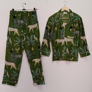 以下が含まれることがあります： 緑色のジャングル柄のパジャマセット。ヒョウ、シマウマ、オニオオハシ、ヤシの木が描かれています。セットには、ボタンダウンの襟付き長袖シャツと、それに合わせたパンツが含まれています。