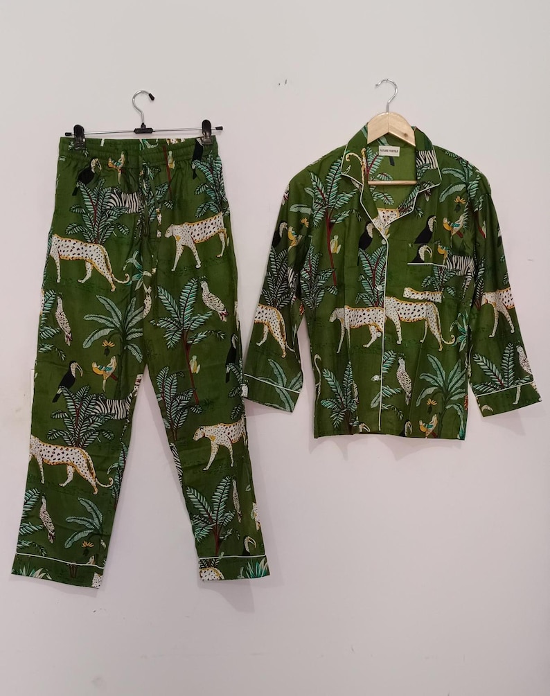以下が含まれることがあります： 緑色のジャングル柄のパジャマセット。ヒョウ、シマウマ、オニオオハシ、ヤシの木が描かれています。セットには、ボタンダウンの襟付き長袖シャツと、それに合わせたパンツが含まれています。