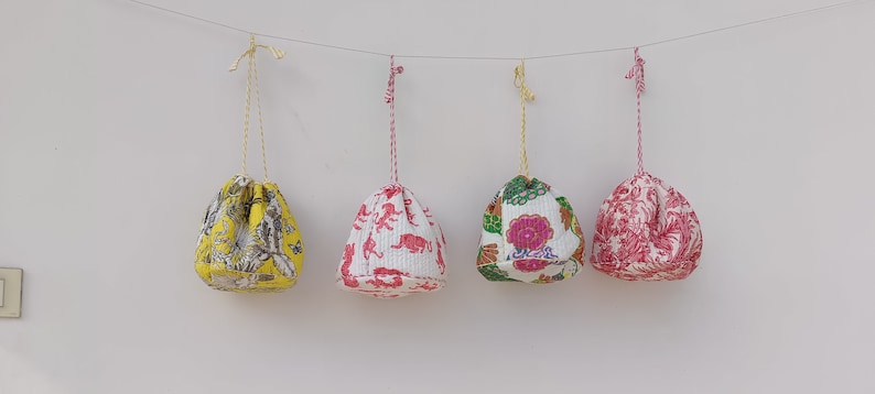 May include: Four drawstring bags with different floral and animal prints hanging from a string. The bags are white with yellow, pink, and green accents.