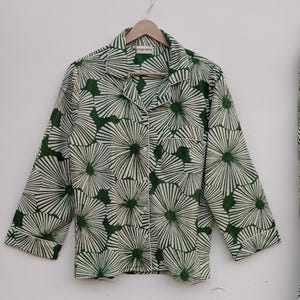 K&ouml;nnte beinhalten: Ein lang&auml;rmliges Hemd in Gr&uuml;n und Wei&szlig; mit einem Blumendruck. Das Hemd hat einen Knopfleisten vorne und eine Tasche auf der linken Seite. Das Etikett auf dem Hemd lautet "Future Textile".