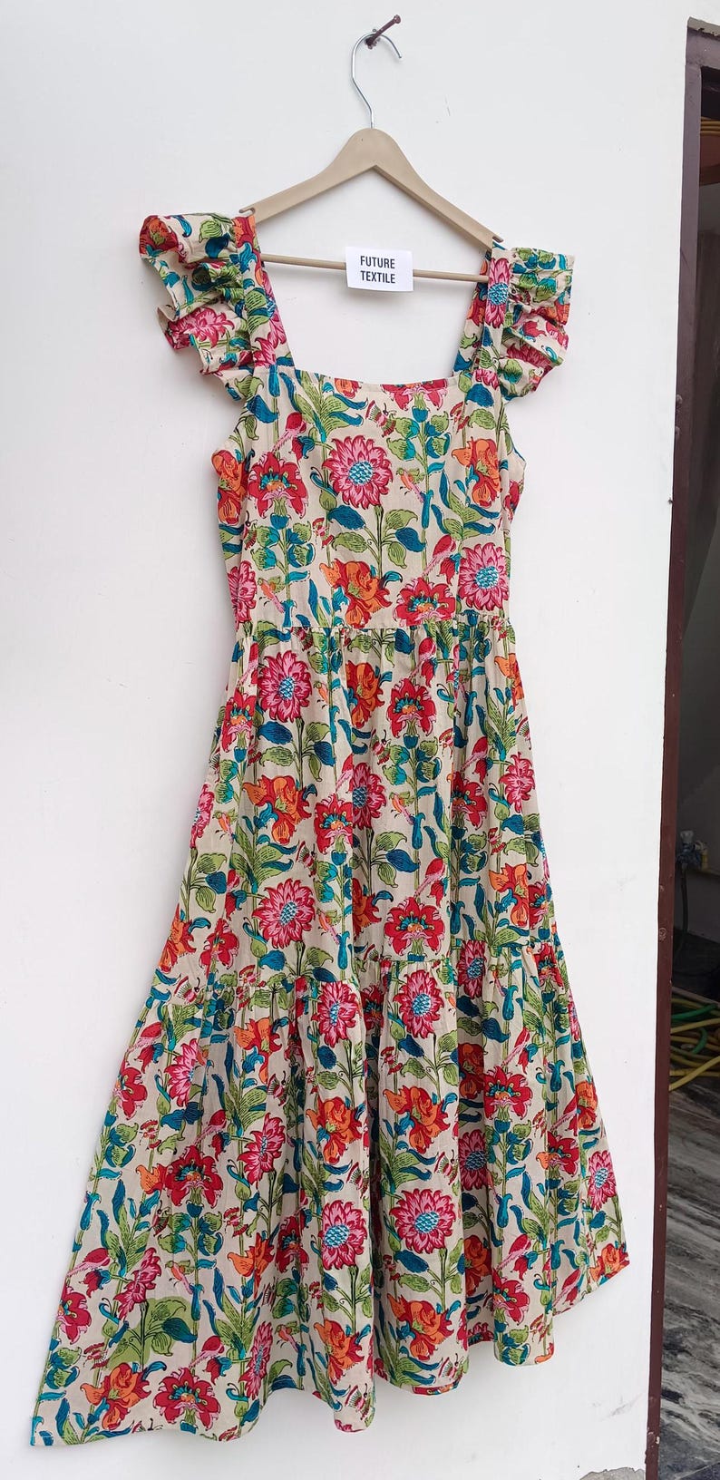 May include: A tiered floral print dress with a square neckline and ruffled cap sleeves. The dress is made of a lightweight fabric and has a relaxed fit. The dress is printed with a colorful floral pattern on a cream background. The dress has a label that says "Future Textile".