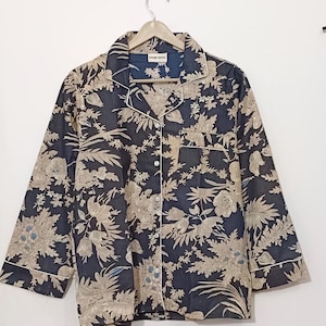 May include: A black button-up shirt with a floral print in beige and blue. The shirt has a collar and long sleeves with a white trim. The label on the shirt reads "FUTURE TEMPLE".