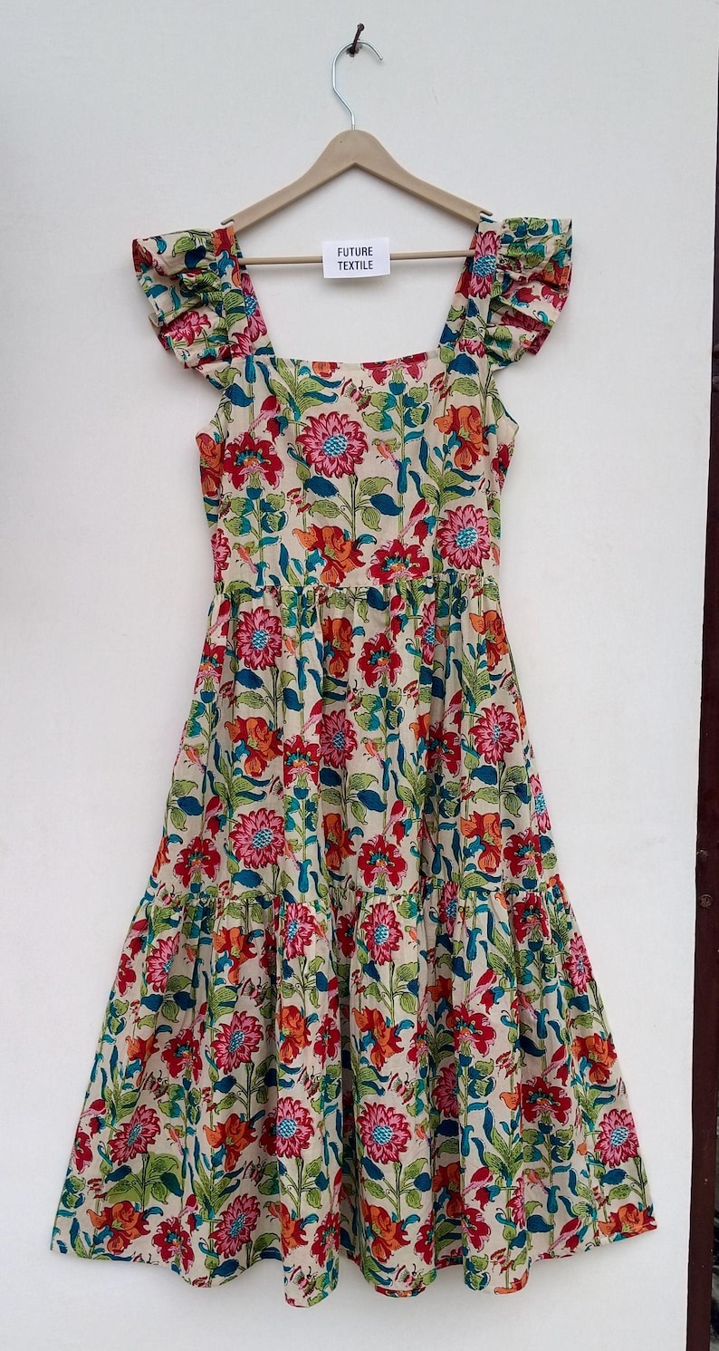 May include: A tiered floral print dress with a square neckline and ruffled cap sleeves. The dress is cream colored with a multi-colored floral pattern. The tag on the dress reads "Future Textile".