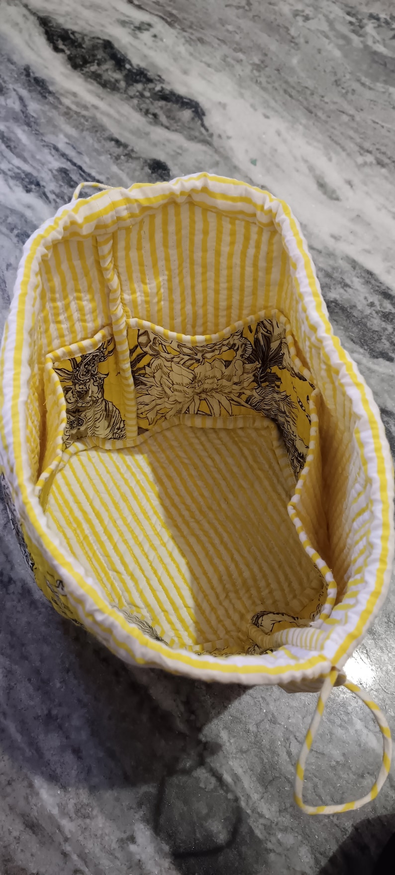May include: Yellow and white striped fabric tote bag with a floral print lining and multiple pockets. The bag has a drawstring closure.