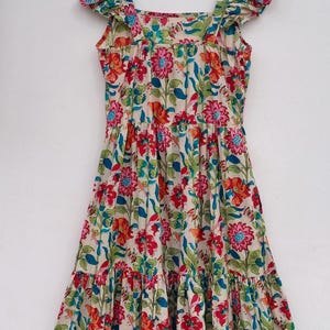 May include: A cream-colored dress with a floral print featuring red, orange, blue, and green flowers. The dress has a square neckline, ruffled straps, and a tiered skirt.