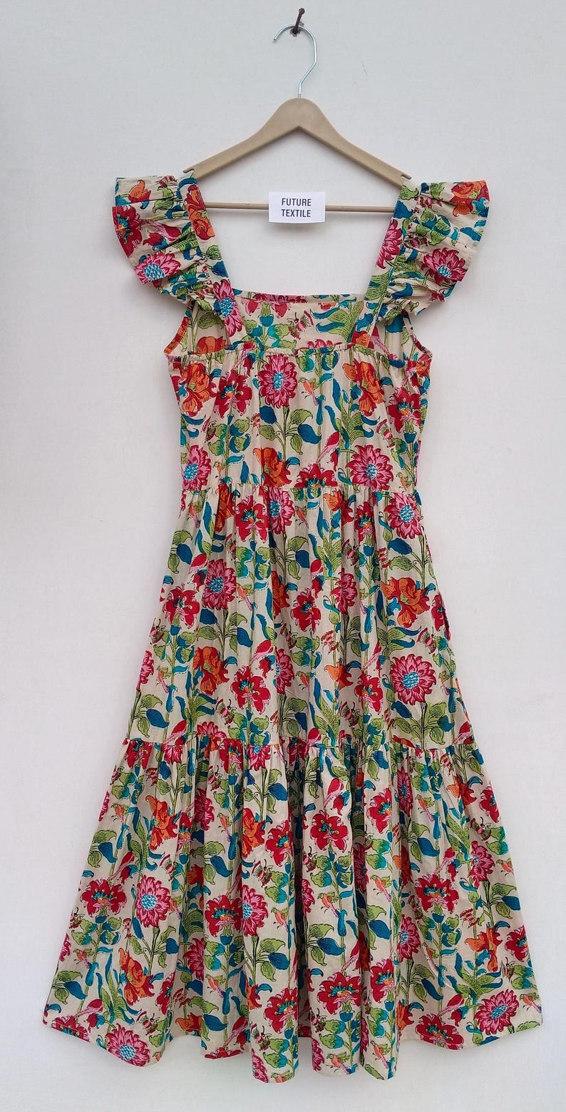 May include: A cream-colored dress with a floral print featuring red, orange, blue, and green flowers. The dress has a square neckline, ruffled straps, and a tiered skirt.