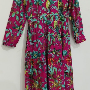 May include: A pink long-sleeved dress with a floral print featuring green leaves and yellow birds. The dress has a button-up front and a gathered skirt. The label on the dress reads "Nature Trails".