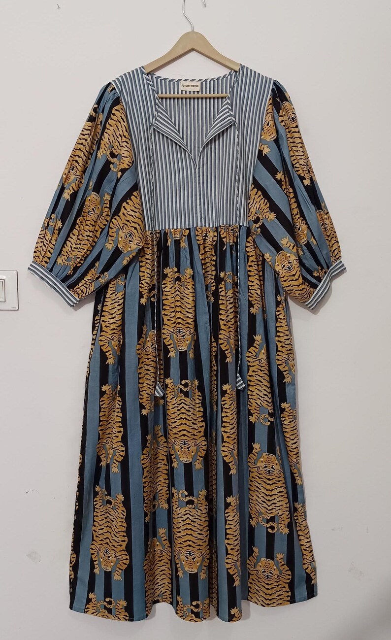 May include: A blue and black striped dress with a tiger print. The dress has a V-neck and 3/4 sleeves. The dress is made of cotton and has a relaxed fit. The dress is hanging on a wooden hanger. The label on the dress says "Future People".