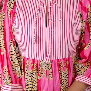 Pu&ograve; includere: Un vestito a righe rosa e bianche con un nodo al collo. Il vestito ha una stampa di tigre sulla gonna e sulle maniche.