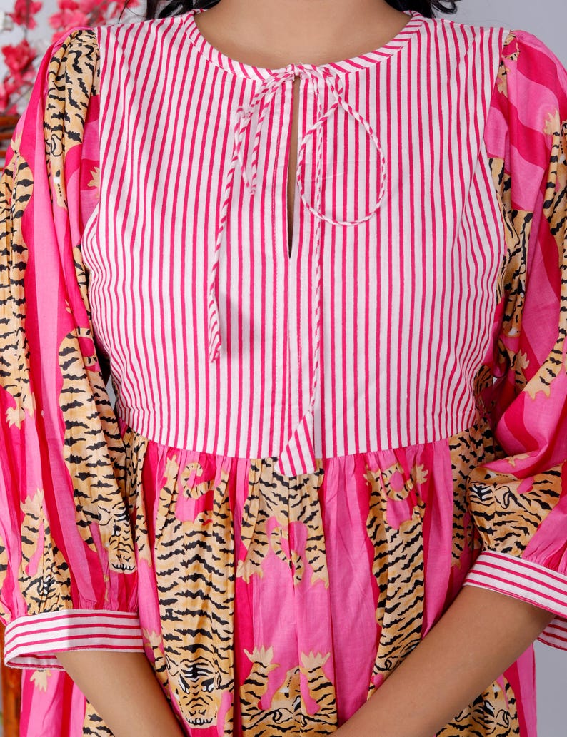 Pu&ograve; includere: Un vestito a righe rosa e bianche con un nodo al collo. Il vestito ha una stampa di tigre sulla gonna e sulle maniche.