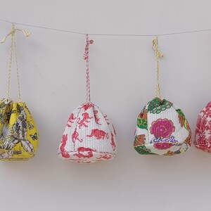 May include: Four drawstring bags hanging from a string. The bags are made of white fabric with different colorful floral and animal prints. The bags are approximately 10 inches in diameter.