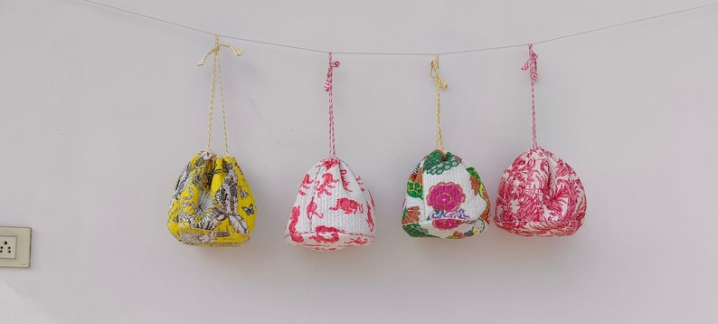 May include: Four drawstring bags hanging from a string. The bags are made of white fabric with different colorful floral and animal prints. The bags are approximately 10 inches in diameter.