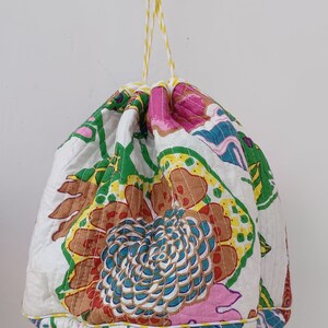 May include: A white drawstring bag with a floral print in shades of pink, green, blue, and yellow. The bag has a yellow and white striped drawstring.