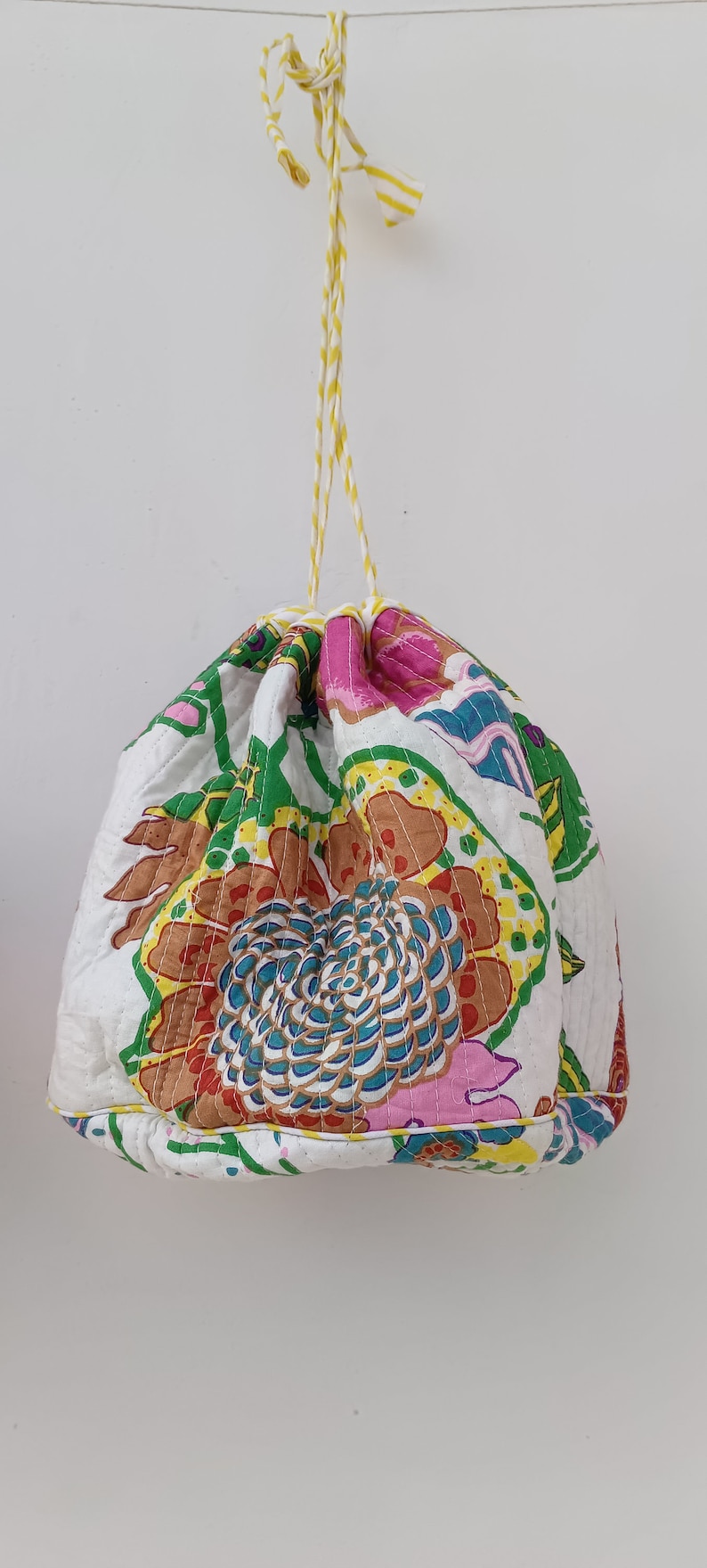 May include: A white drawstring bag with a floral print in shades of pink, green, blue, and yellow. The bag has a yellow and white striped drawstring.