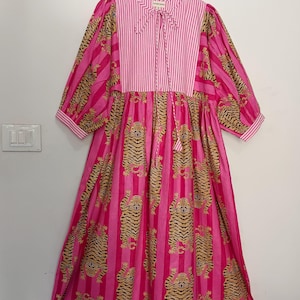 Pu&ograve; includere: Un vestito a righe rosa e bianche con una stampa di tigre. Il vestito ha un nodo al collo ed &egrave; fatto di cotone.