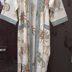 May include: A white cotton robe with a green and white striped trim. The robe has a floral print of palm trees and flowers.