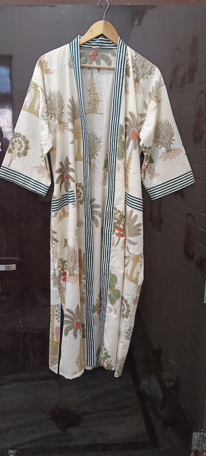 May include: A white cotton robe with a green and white striped trim. The robe has a floral print of palm trees and flowers.