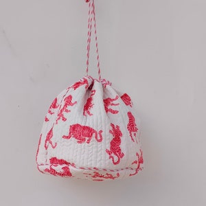 May include: White drawstring bag with pink tiger print. The bag is hanging from a white string.