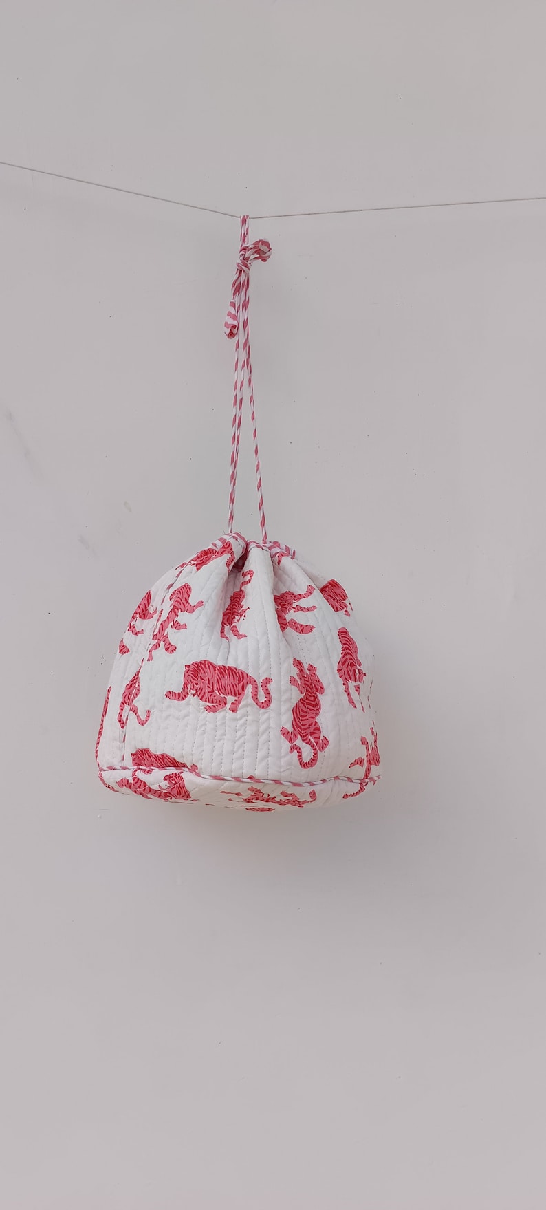 May include: White drawstring bag with pink tiger print. The bag is hanging from a white string.