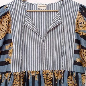 May include: A blue and white striped dress with a V-neck and short sleeves. The sleeves and bottom of the dress feature a tiger print pattern. The dress has a tag that reads "FUTURE TEXTILE".