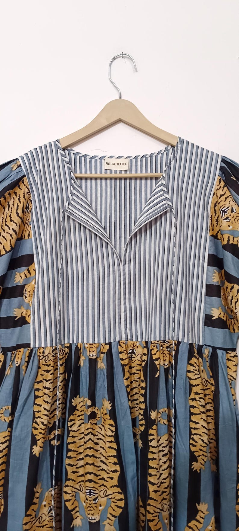 May include: A blue and white striped dress with a V-neck and short sleeves. The sleeves and bottom of the dress feature a tiger print pattern. The dress has a tag that reads "FUTURE TEXTILE".