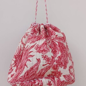 May include: A white drawstring bag with a pink floral pattern. The bag has a red and white striped drawstring.