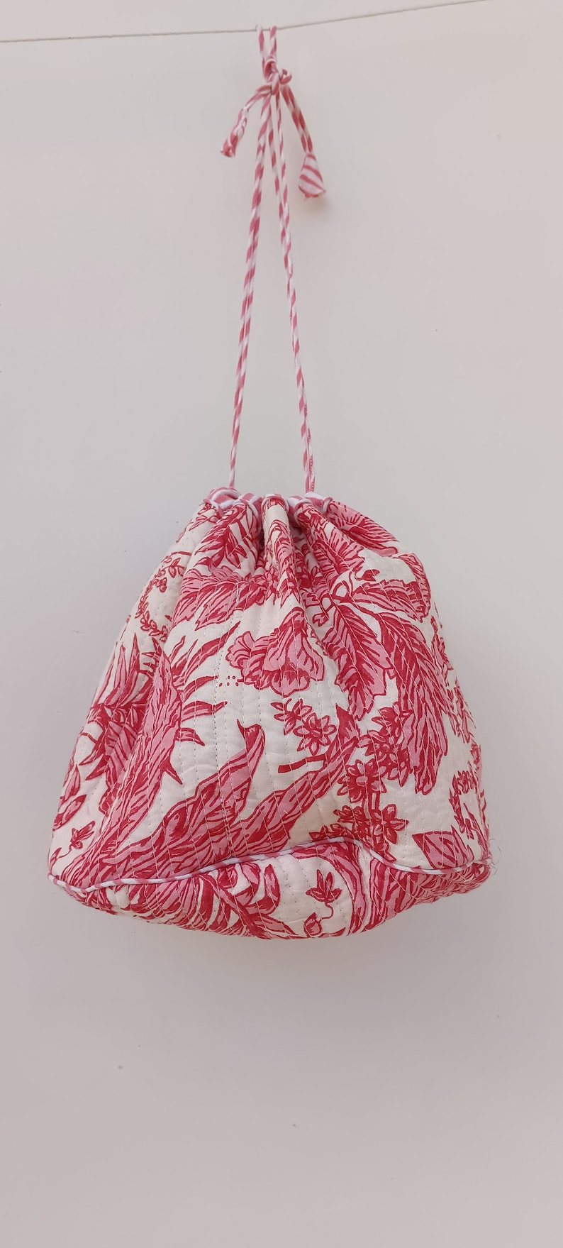 May include: A white drawstring bag with a pink floral pattern. The bag has a red and white striped drawstring.