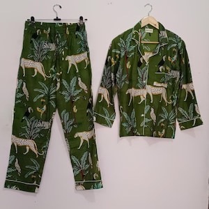以下が含まれることがあります： 緑色のジャングル柄のパジャマセット。ヒョウ、オニオオハシ、ヤシの木がプリントされています。セットには、ボタンダウンカラーの長袖シャツと、それに合わせたパンツが含まれています。