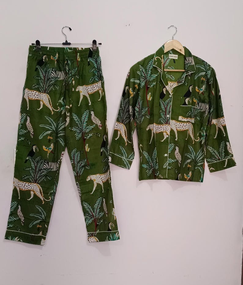 以下が含まれることがあります： 緑色のジャングル柄のパジャマセット。ヒョウ、オニオオハシ、ヤシの木がプリントされています。セットには、ボタンダウンカラーの長袖シャツと、それに合わせたパンツが含まれています。