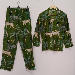 以下が含まれることがあります： 緑色のジャングル柄のパジャマセット。ヒョウ、オニオオハシ、ヤシの木、シマウマが描かれています。セットには、ボタンダウンの襟付き長袖シャツと、それに合わせたパンツが含まれています。