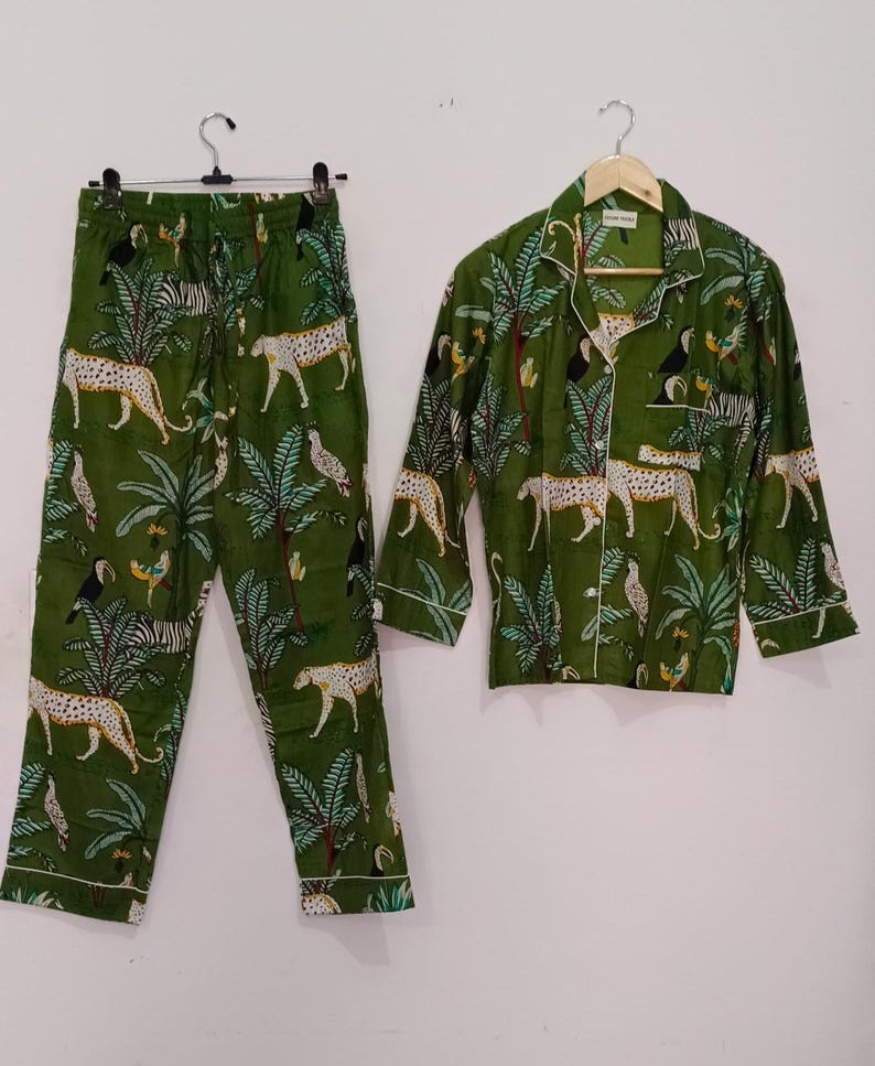 以下が含まれることがあります： 緑色のジャングル柄のパジャマセット。ヒョウ、オニオオハシ、ヤシの木、シマウマが描かれています。セットには、ボタンダウンの襟付き長袖シャツと、それに合わせたパンツが含まれています。