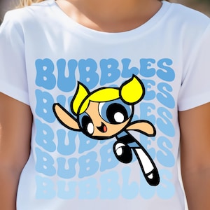 May include: White t-shirt with a cartoon image of Bubbles from the Powerpuff Girls. The shirt has a blue and white repeating pattern of the word "Bubbles".