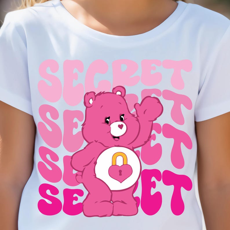 May include: White t-shirt with a pink Care Bear wearing a heart with a lock on it. The text "SECRET" is repeated in pink and white on the shirt.