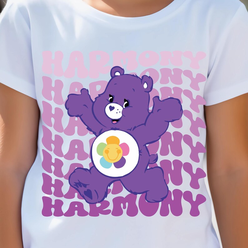 May include: A white t-shirt with a purple Care Bear wearing a rainbow flower on its belly. The bear is running and the word "HARMONY" is repeated in pink and purple letters on the shirt.